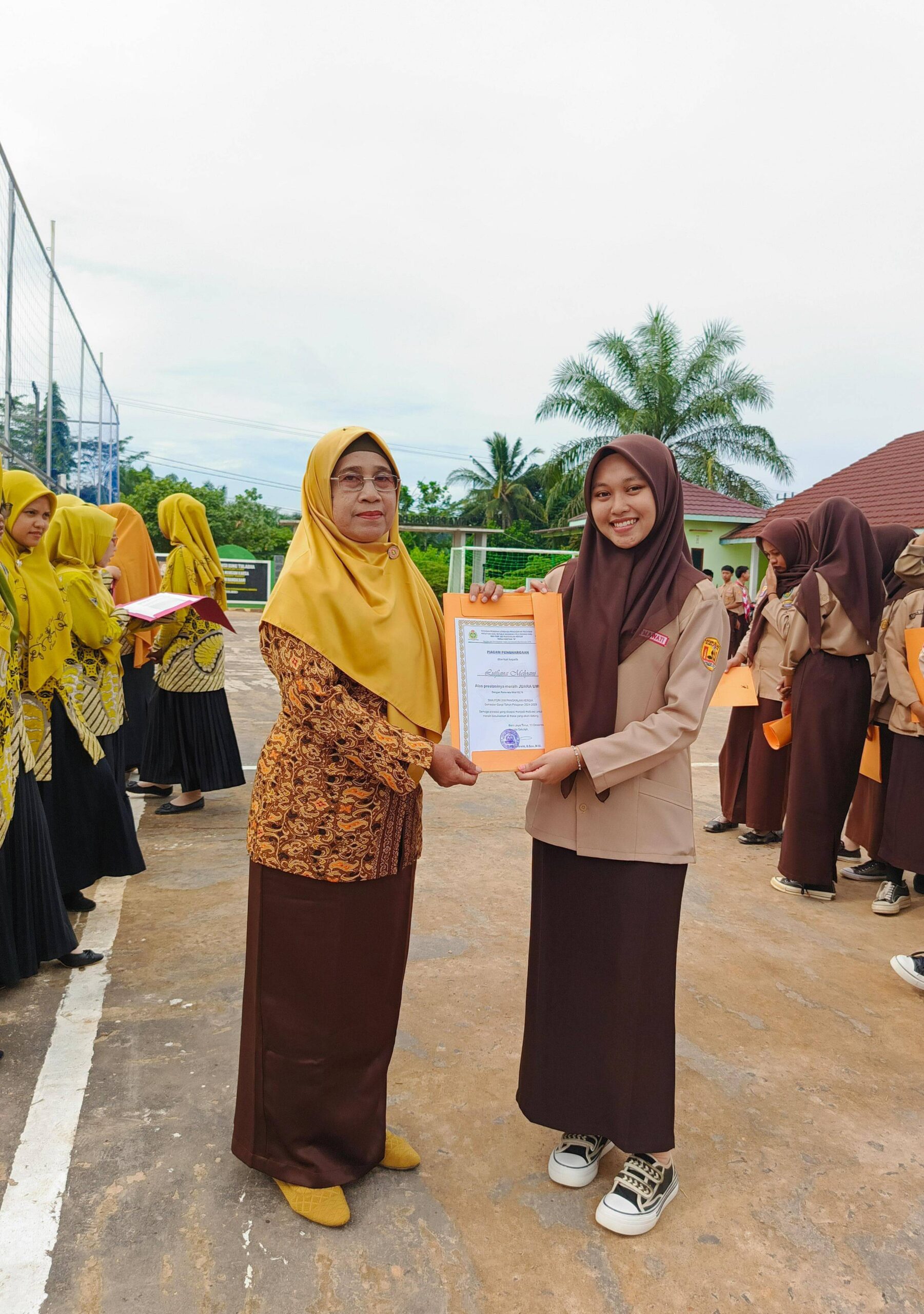 Lutfiana Melyani, siswa berprestasi dari Kelas XII IPS 1, memegang piala juara umum dengan latar belakang sekolah SMA PGRI 268 Pangkalan Kersik